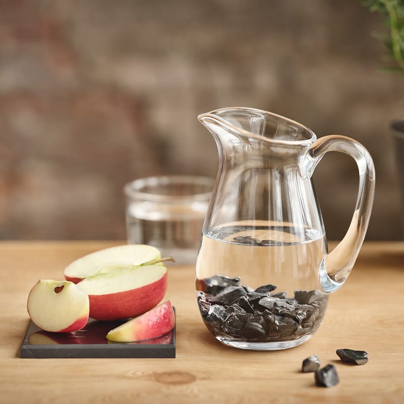 Wasserkrug mit Arielle-Wassersteinen und frisches Obst auf einer Lotte-Lebensmittelplatte von Beyond Matter – für energetisierte Lebensmittel und Trinkwasser.