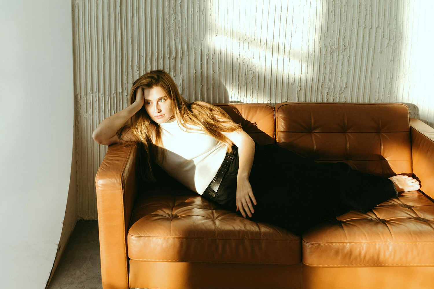 Frau liegt nachdenklich auf einem Sofa im Sonnenlicht – Ruhephase während körperlicher Anpassungs- oder Regenerationsprozesse.