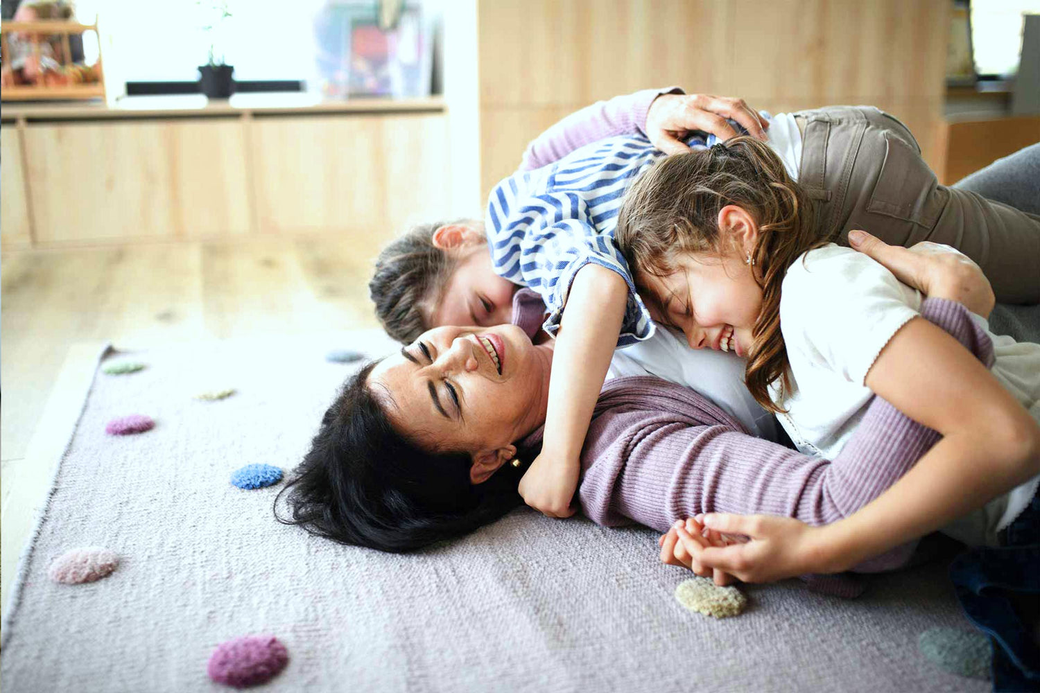 Mutter spielt mit zwei Kindern auf dem Boden in einer hellen Wohnumgebung – Sinnbild für Allgegenwärtigkeit von EMF im Alltag.