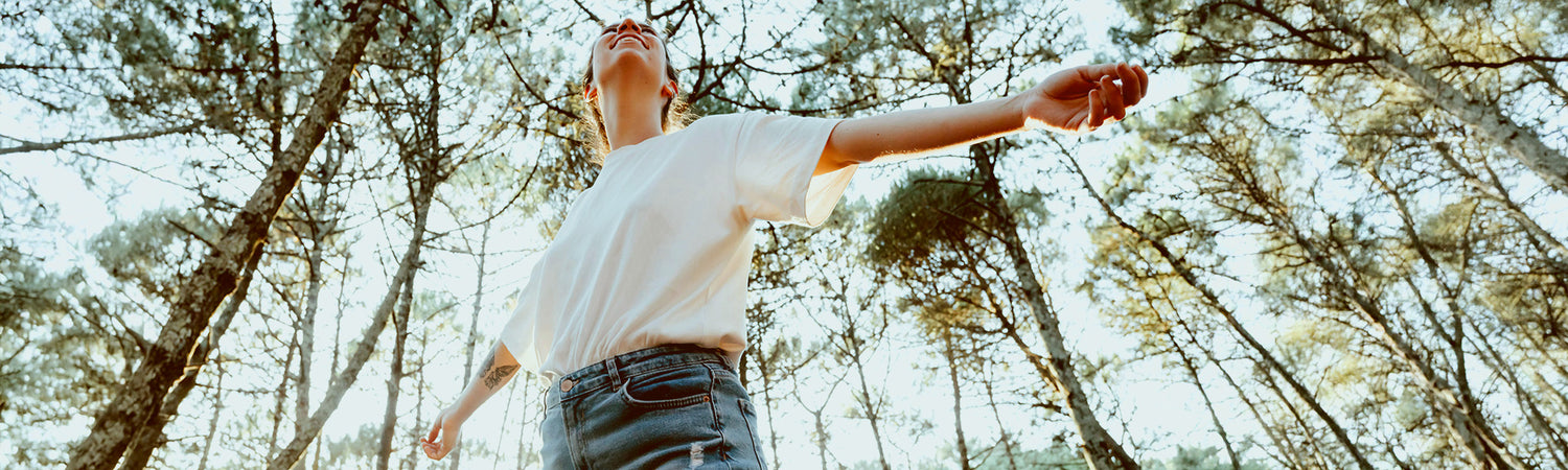 Junge Frau mit ausgebreiteten Armen im Wald – Sinnbild für Freiheit, Leichtigkeit und Beschwerdefreiheit.