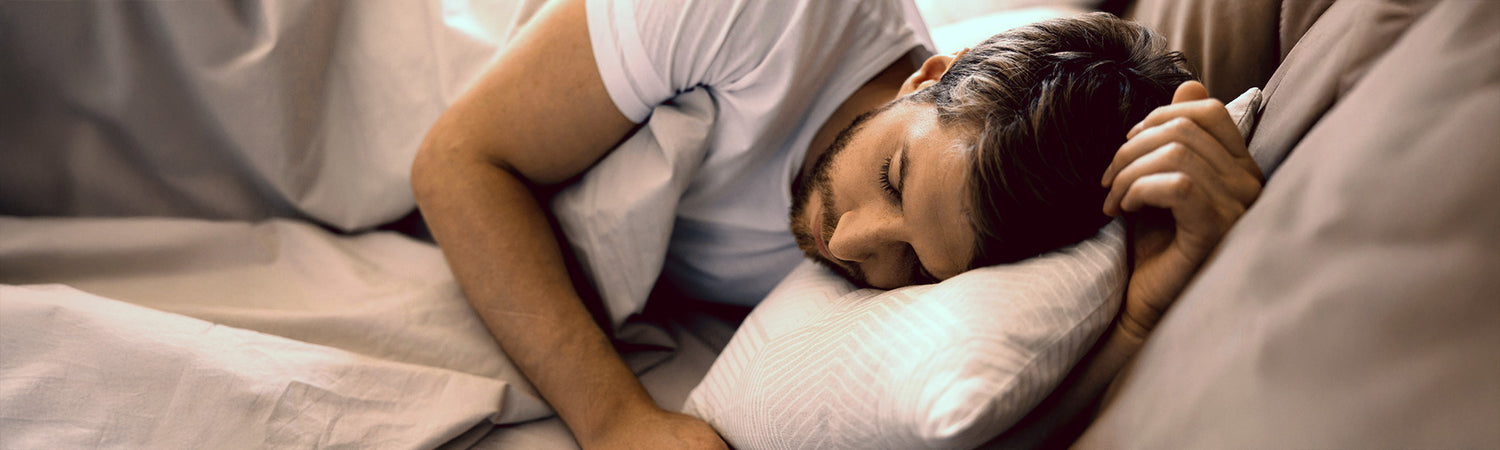 Mann liegt im Bett – Sinnbild für Schlaf, Erholung und Regenerationsfähigkeit.