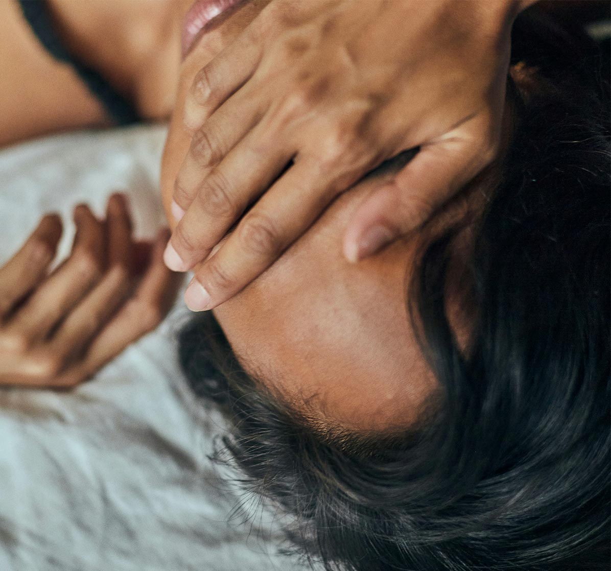 Frau im Bett liegend mit Händen vor den Augen – Sinnbild für Erschöpfung