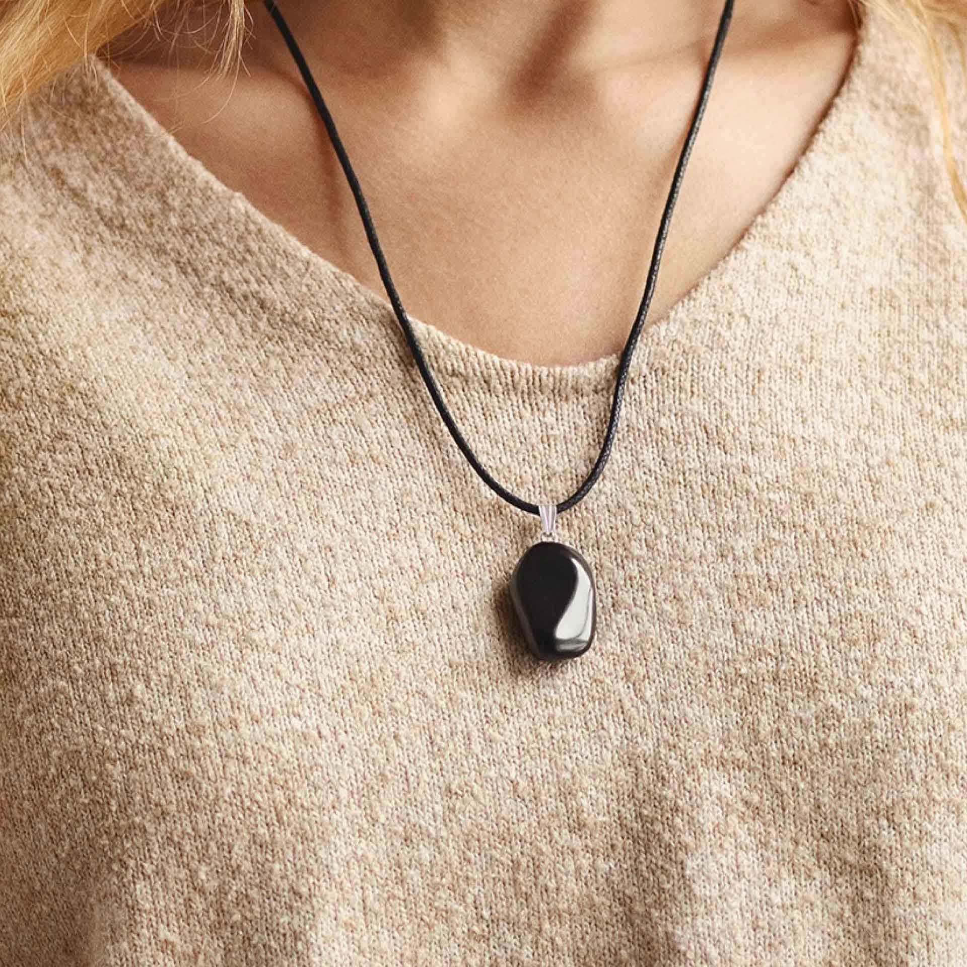 Schwarzer Anhänger an einer Kette – auf Herzhöhe, getragen im Alltag.
