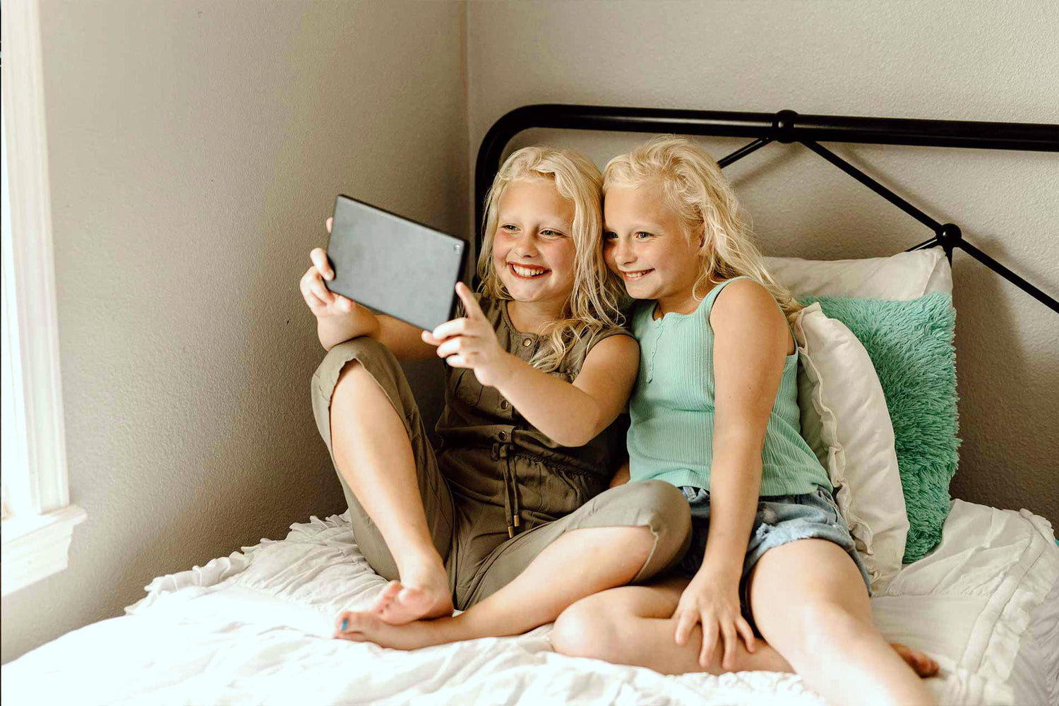 Zwei Kinder nutzen gemeinsam ein Tablet auf dem Bett – Mediennutzung im Kindesalter und mögliche Gesundheitsaspekte von EMF.