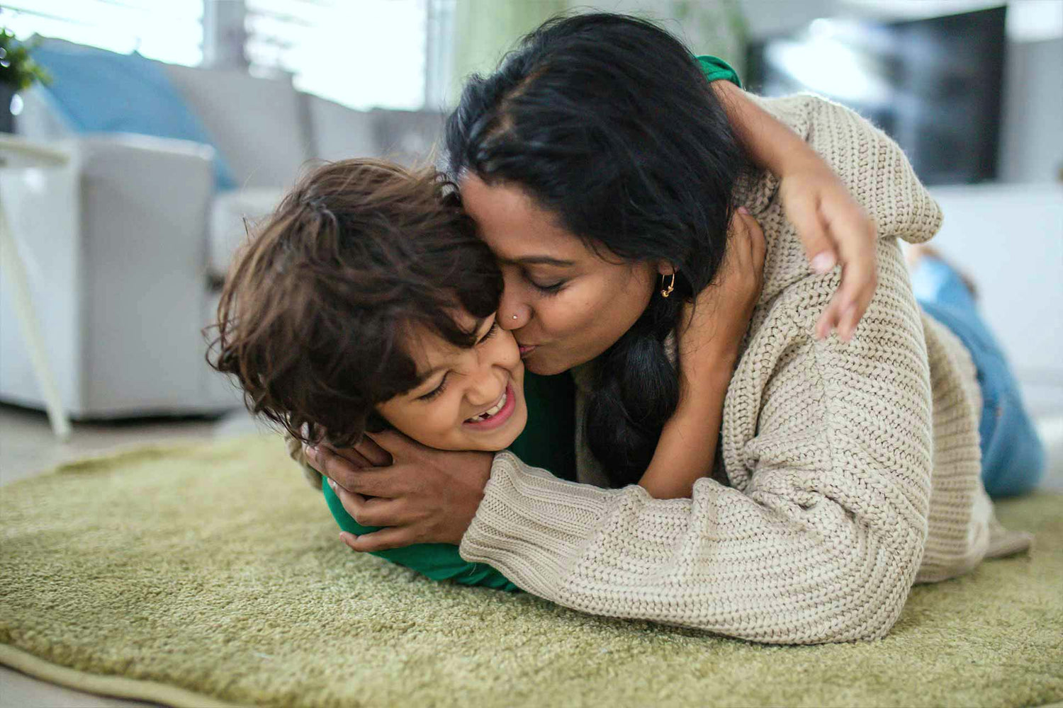 Mutter umarmt ihr Kind liebevoll im Wohnzimmer und schafft einen Moment von Nähe und Geborgenheit.
