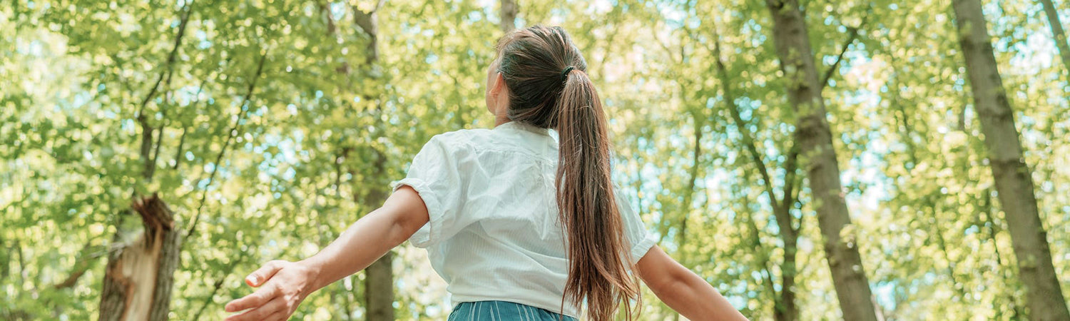 Person mit ausgebreiteten Armen im Wald – Sinnbild für Freiheit, Zukunft und eine bewusste Verbindung von Mensch und Technologie.