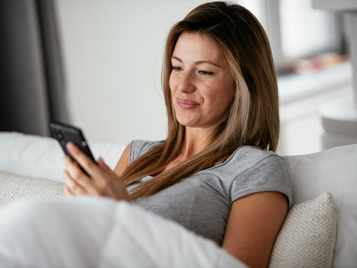 Frau liegt entspannt im Bett und nutzt ihr Smartphone – ruhiger Moment im Alltag.