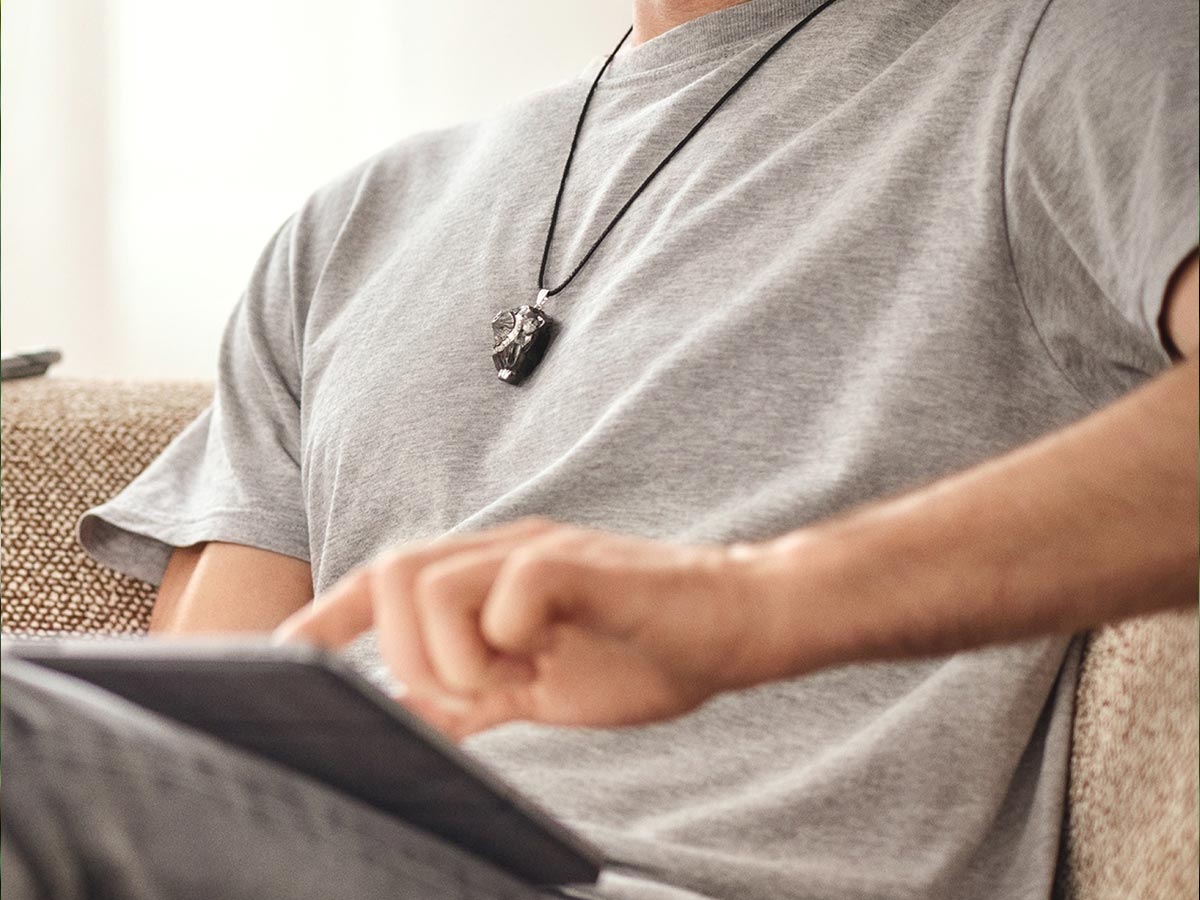 Mann sitzt entspannt, trägt Anhänger Sol und nutzt ein Tablet – konzentrierter Moment in ruhiger Umgebung.