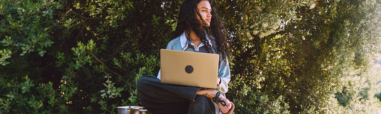 Frau mit Laptop unter einem Baum – Sinnbild für alltägliche Anwendung der Produkte von Beyond Matter.