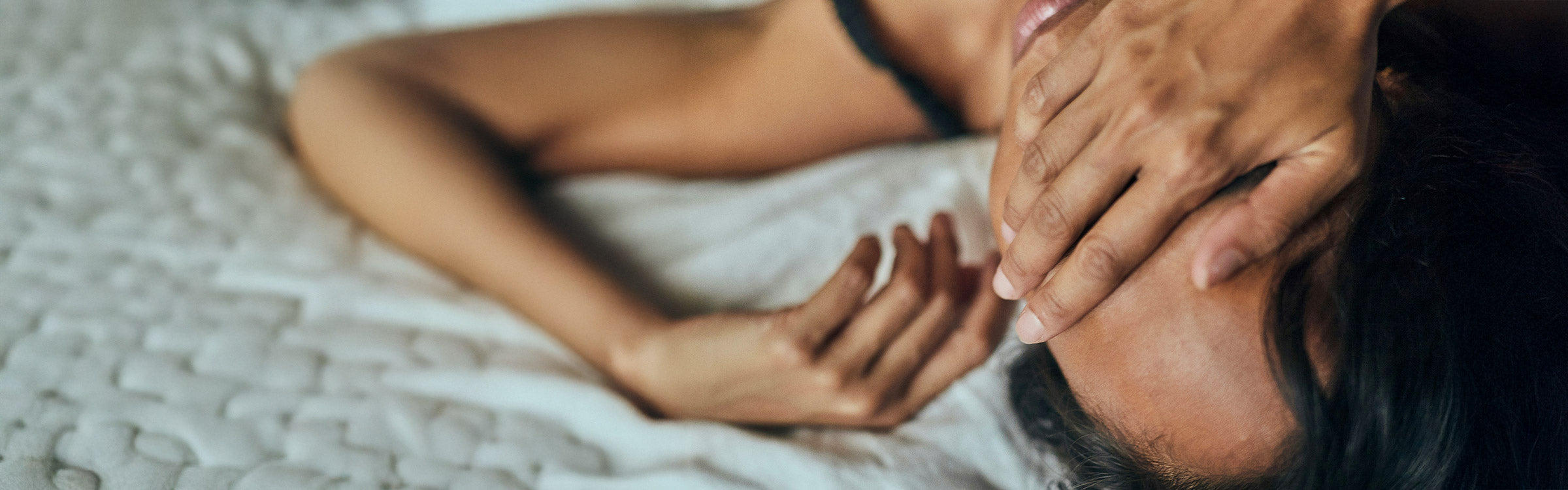 Frau im Bett liegend mit Händen vor den Augen – Sinnbild für Erschöpfung