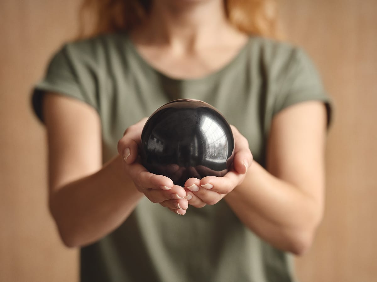 Kugel Samson aus EssenceX-Schungit von Beyond Matter wird achtsam in den Händen gehalten.