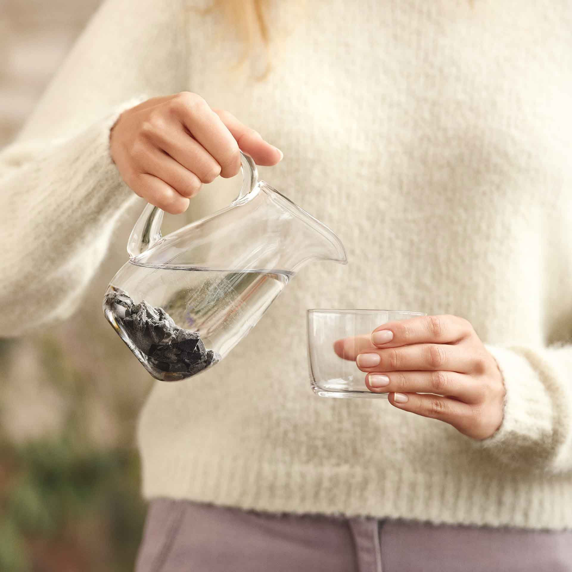 Einschenken von Wasser aus einem Krug mit Arielle-Steinen – alltägliche Anwendung für bewussten Wassergenuss.